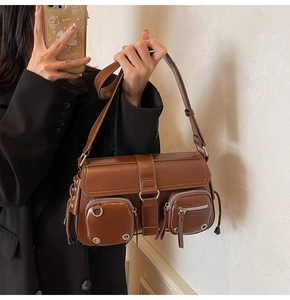 Detail of dark brown leather baguette bag featuring zip pockets and adjustable strap