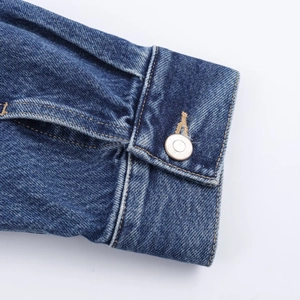 Close-up of denim jacket cuff showing silver metal button and high-quality stitching