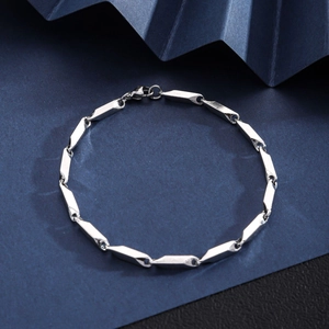 Close-up of a silver stainless steel Cuban link bracelet with lobster clasp on textured paper