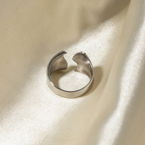 Gros plan détaillé d'une bague ouverte irrégulière argentée sur de la soie beige