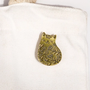 Gros plan d'une broche chat en bronze avec relief floral sur un petit sac en toile