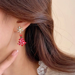 Close-up of snowflake stud and red Christmas tree earring worn on a model's ear