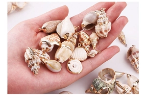 Hand holding natural shell pendants with gold plated edges for DIY jewelry making
