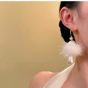 Close-up of elegant pearl and white pom-pom drop earrings worn by a model on plain background