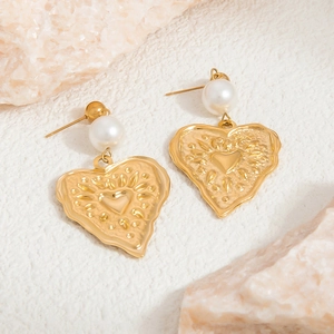 Exaggerated 18K gold heart earrings with white pearls on a textured rock background