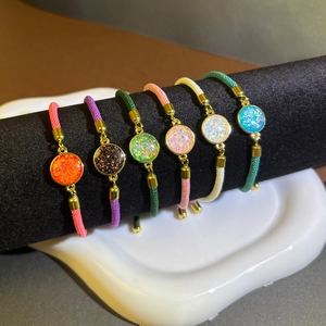 Detailed view of six colorful adjustable braided rope bracelets with shiny metal discs
