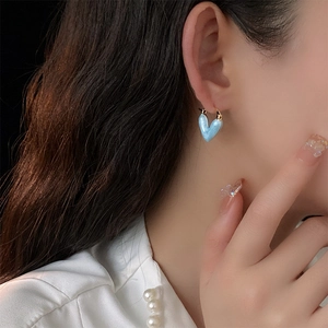 Gros plan d'une boucle d'oreille cœur bleu plaqué or portée sur une oreille