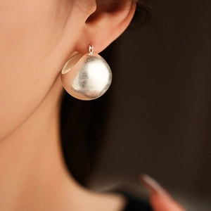 Close-up of a silver spherical earring with a matte metallic texture on a model