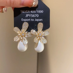 Close-up of sparkling floral earrings with teardrop pearls on a silver 925 jewelry tag