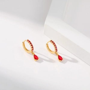 Close-up of 18K gold brass teardrop earrings with inlaid red zircon on a white stand