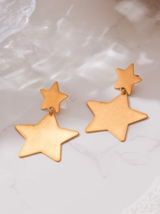 Detail of star-shaped earrings with brushed gold finish on white marble background