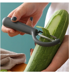 Close-up of grey handle peeler slicing a fresh cucumber in a home kitchen setting