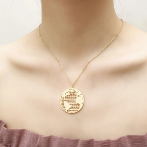 Close-up of a gold cutout world map pendant on a thin chain worn by a female model