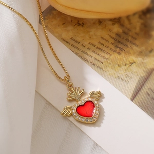 Detail view of a gold-plated winged heart necklace with red stone on vintage paper
