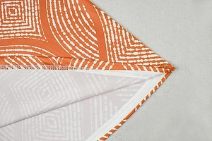 Detailed close-up of orange geometric print fabric and precise overlock stitching detail