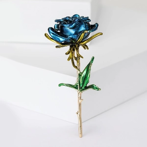 Elegant metallic blue rose brooch with gold stem and green leaves on a white podium