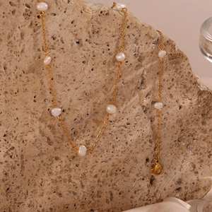 Detail of a gold stainless steel chain necklace with freshwater pearls on a rock background
