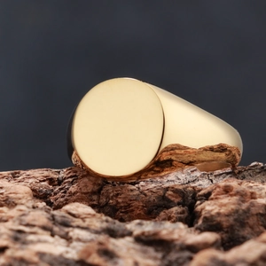 Polished gold round signet ring displayed on natural wood bark against dark background