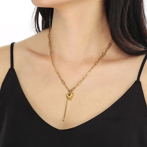 Gros plan du collier en acier doré avec pendentif cœur et pompon porté par un mannequin