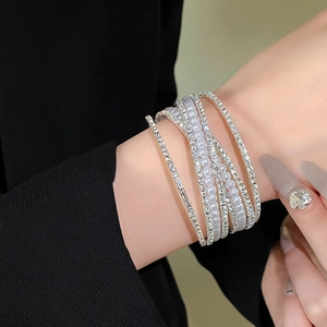 Detail van een gelaagde zilveren armband met glinsterende steentjes en parels om de pols