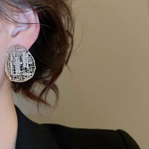 Détail de boucles d'oreilles géométriques argentées avec zircons sur un modèle féminin