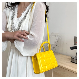Détail d'un sac à main jaune avec motif cœur embossé porté par un mannequin en robe blanche