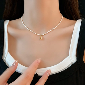 Detail of bohemian necklace with white seed beads and a gold seashell pendant on model