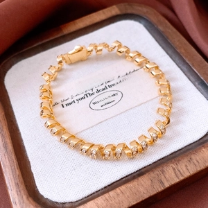 Macro shot of gold twist chain bracelet with sparkling crystals on wooden jewelry tray