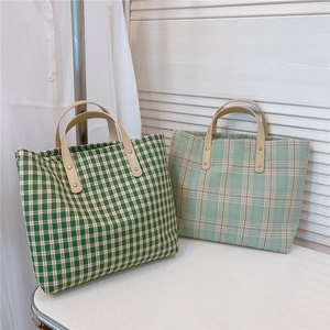 Close-up of green plaid tote bags with cream leather handles on a white table