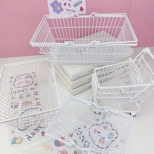 Desktop setup with white wire storage baskets and mini shopping cart on a pink background
