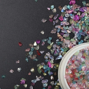 Irregular iridescent glass fragments for DIY nail art in white jar on black background