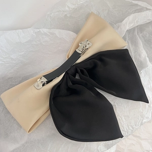 Close-up of dual-tone beige and black satin bow hair clip with a metal spring fastener