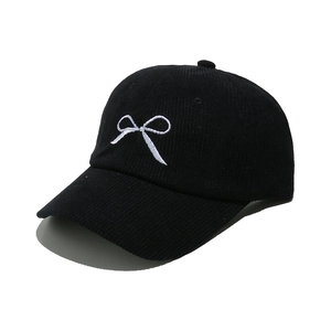 Close-up of embroidered white bow on black corduroy baseball cap showing fabric texture