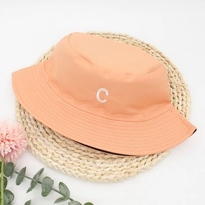 Detail of light orange bucket hat with white 'C' embroidery on a woven mat