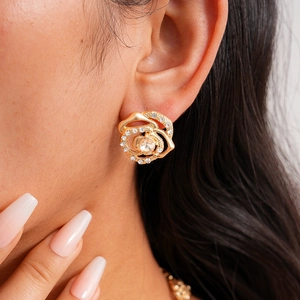Close-up of gold hollow flower earrings with white crystals worn by a model