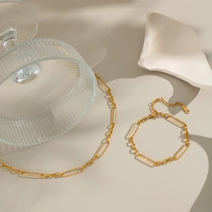 Detailed view of golden paperclip chain necklace and bracelet set on an artistic background