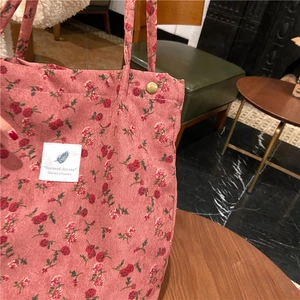 Detalle de textura de bolso tote de pana rosa con estampado floral rojo y botón metálico