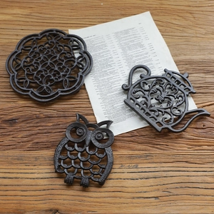 Rustic cast iron trivets in owl and teapot shapes on a vintage wooden table surface