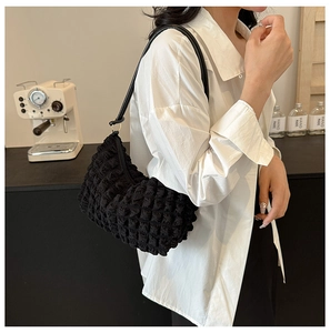 Detailed view of black textured bubble fabric shoulder bag worn by model in a chic setting