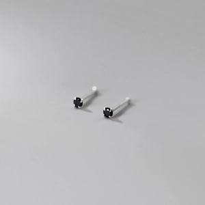 Macro shot of minimalist silver studs with four-prong set round black gemstones
