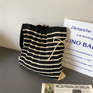 Detail of striped knit tote bag featuring a pleated texture and beige bow decoration