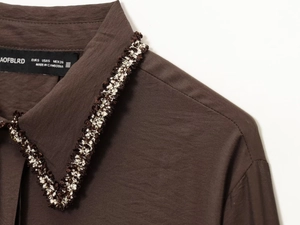 Detail of shirt collar with intricate black, white and gold woven braided trim finish