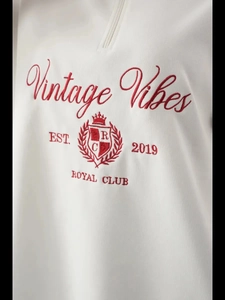 Nahaufnahme des weißen Sweatshirts mit roter Vintage-Stickerei und halbem Reißverschluss