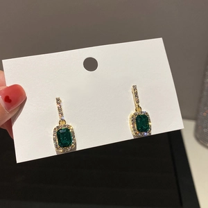 Macro view of emerald green square stud earrings with gold plating and paved crystals