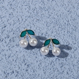 Detailed view of cherry earrings with white pearls and green enamel leaves on a stone background