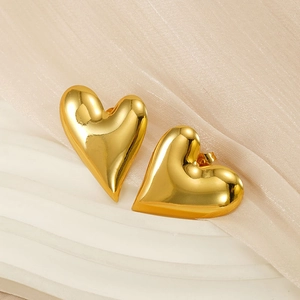 Close-up of polished gold-finished heart stud earrings on beige fabric texture