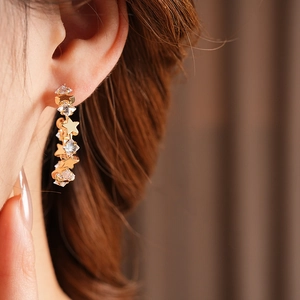 Close-up of golden star-shaped C-hoop earring with sparkling zircons on a model