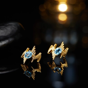 Macro view of gold earrings featuring sky blue oval-cut gemstones on black reflection