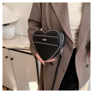 Detail of heart-shaped black leather bag with double zippers and stylish cross-body strap
