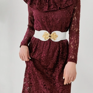 Detail of white elastic waist belt featuring a gold floral buckle on a burgundy dress